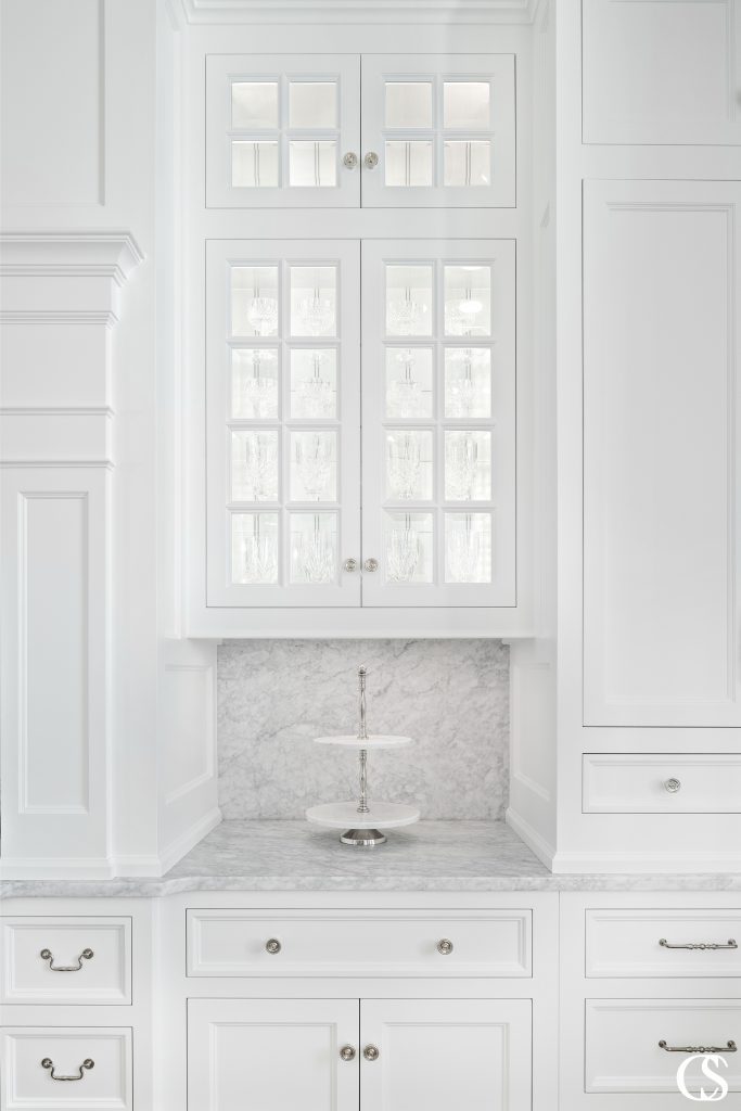 Instead of creating a full wall of cabinetry, the white custom cabinets in this kitchen open up for a little display area and let the room relax in a bit of luxury.