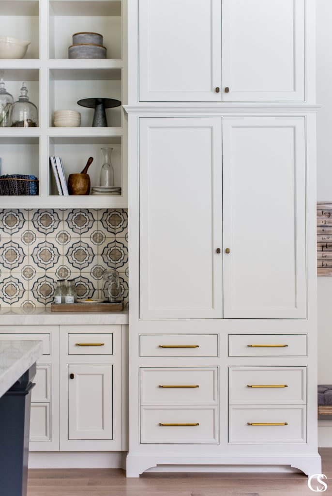 We love the combination of hardware styles mixed with a detailed tile backsplash in this set of custom white kitchen cabinets.